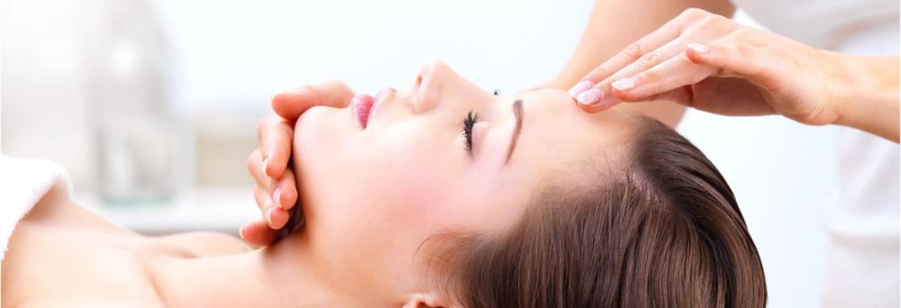 Frau liegt entspannt auf einer Liege, während eine Kosmetikerin sanft Stirn und Kinn berührt – Symbolbild für kosmetische Behandlungen.