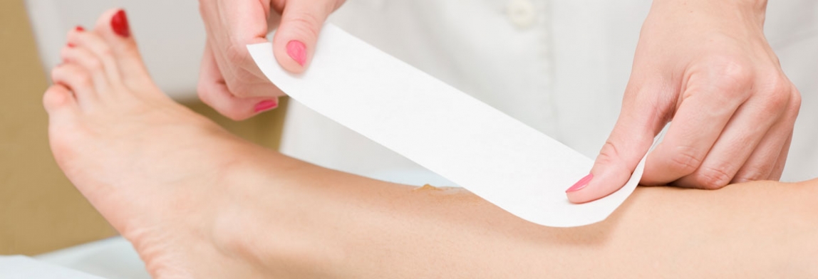 Enthaarungsbehandlung am Bein: Eine Kosmetikerin zieht einen Wachsstreifen von der Haut einer liegenden Person ab