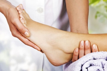 Eine Person führt eine Fußpflege durch und hält sanft den Fuß einer anderen Person, der in ein Handtuch gewickelt ist.