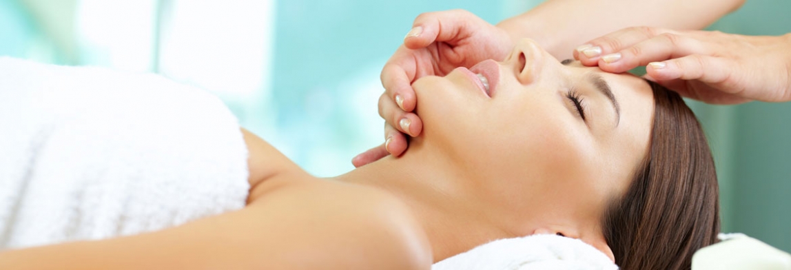 Frau liegt entspannt auf einer Liege und erhält eine sanfte Gesichtsbehandlung mit Massage in heller Spa-Umgebung